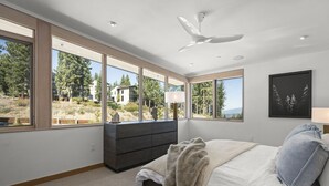Un dormitorio con un ventanal grande, una cama, un tocador y un ventilador de techo.