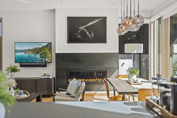 Ein modernes Wohnzimmer mit Kamin, Fernseher und Essbereich.