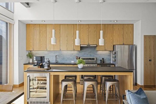 Une cuisine moderne avec des meubles en bois, des appareils en acier inoxydable et un îlot central doté de tabourets de bar.