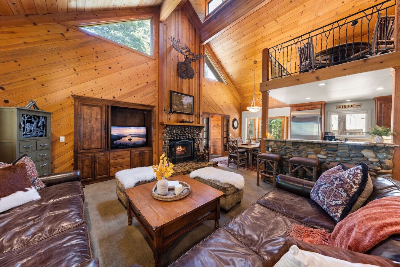 A rustic cabin interior with a stone fireplace, leather furniture, and a dining area.