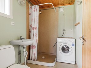 A compact bathroom with a sink, toilet, shower, and washing machine.