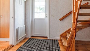 Una escalera de madera con barandilla, una puerta blanca con ventanal y un felpudo estampado en el suelo.