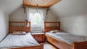 Une chambre avec deux lits en bois, une fenêtre avec des rideaux et un plafond en pente.