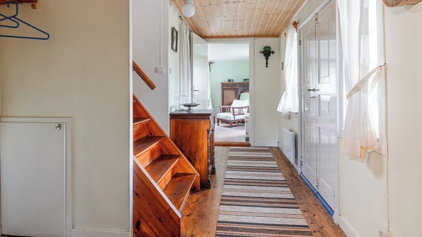 Un escalier en bois mène à une chambre à coucher qui contient un lit, une commode et une fenêtre avec des rideaux.