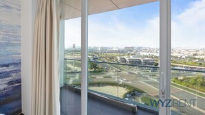 Een moderne hotelkamer met een ruim balkon, stadszicht en een raam met gordijnen.