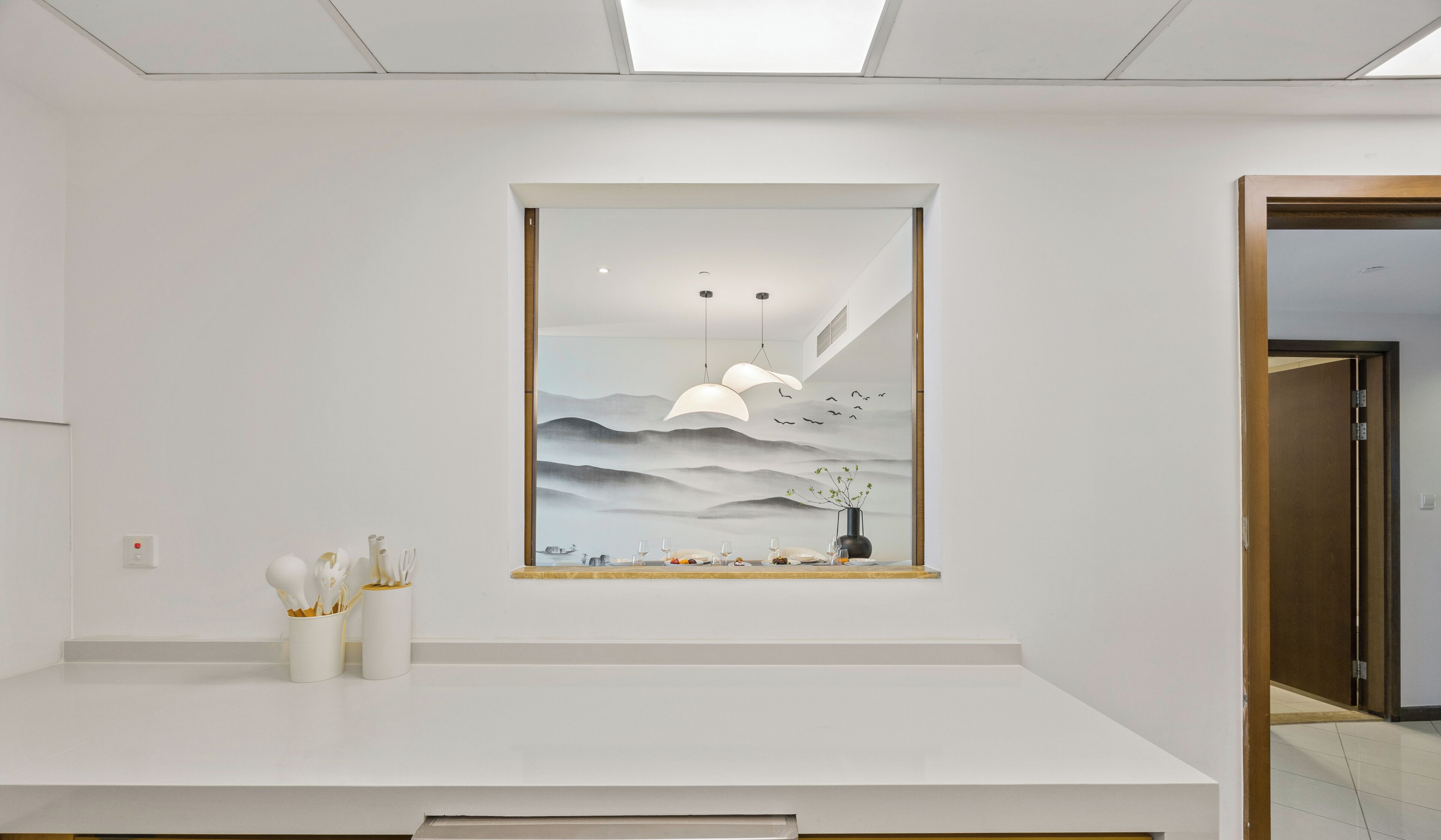 A modern interior with a minimalist design, featuring a wall-mounted artwork, a white reception desk, and a door leading to another room.