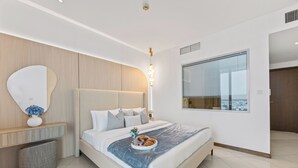 Een moderne slaapkamer met een groot bed, een nachtkastje met een bloevas, een spiegel aan de muur en een raam met jaloezieën.