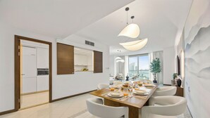 Een moderne eethoek met een lange houten tafel voor zes personen, witte stoelen en uitzicht op de stad door grote ramen.