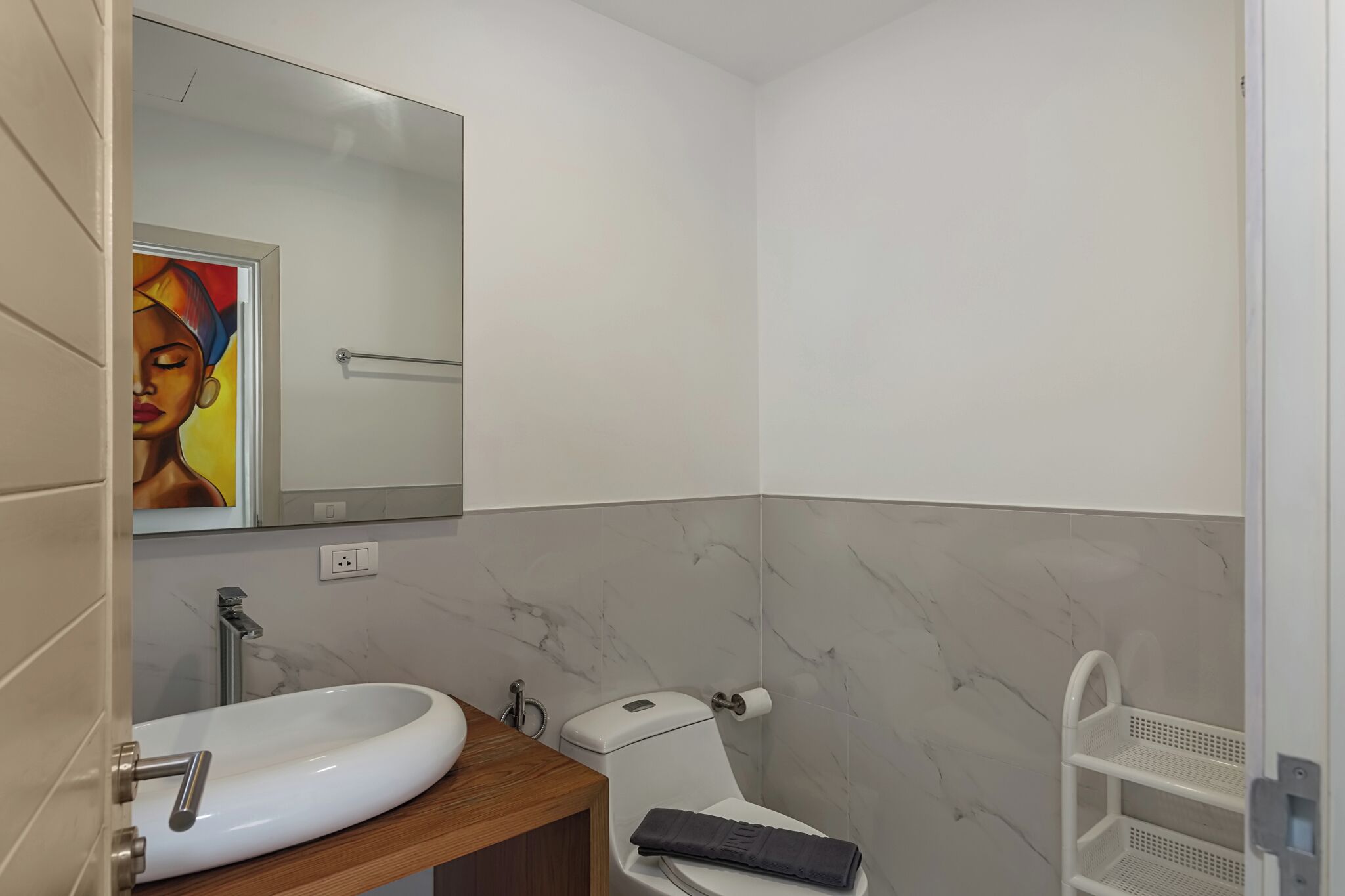 A modern bathroom with a marble backsplash, a white sink, a toilet, and a white shelf unit.