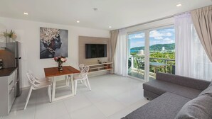 Ein modernes Wohnzimmer mit grauem Sofa, einem Esstisch mit Stühlen, einem Flachbildfernseher und einem Balkon mit Blick auf die Stadt.