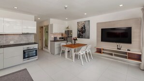 Eine moderne Küche mit weißen Schränken, einem eingebauten Ofen und einem Essbereich mit Holztisch und weißen Stühlen.