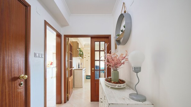 A hallway with a wooden door, a white console table with a vase and a lamp, and a mirror on the wall.