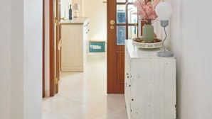 A hallway with a white wooden cabinet, a door leading to a kitchen, and a wall-mounted light fixture.