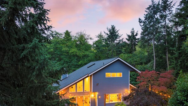 Una casa moderna con terraza, rodeada de un bosque denso.