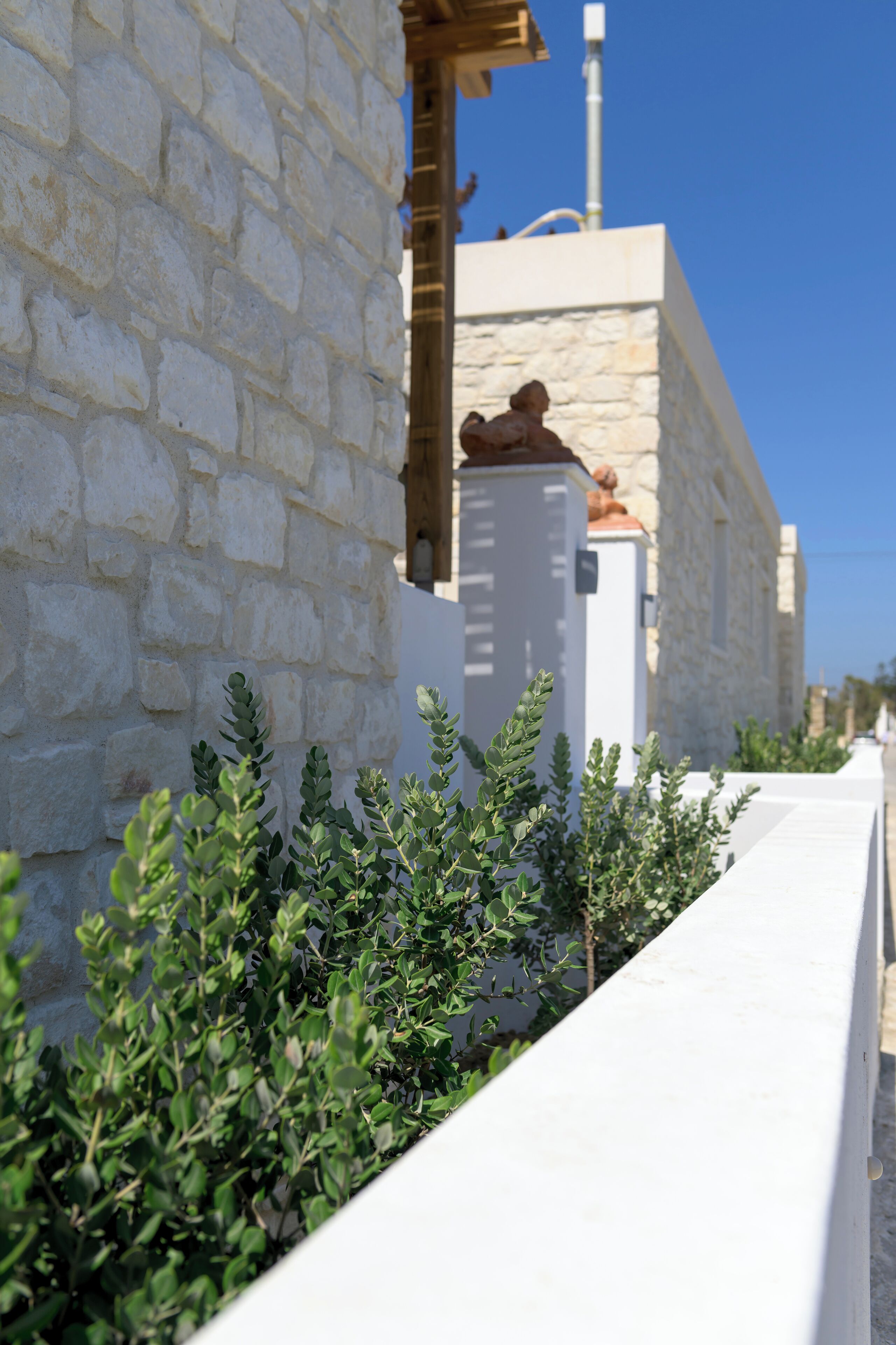 A stone building with a white wall and a small garden area with green shrubs.