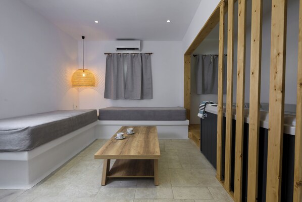 A compact room with a wooden table, a bench, a hanging light fixture, and a kitchenette area.
