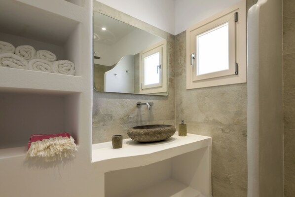 A bathroom with a stone sink, a mirror, and shelves with towels. - Stone Whisper (Naxos)