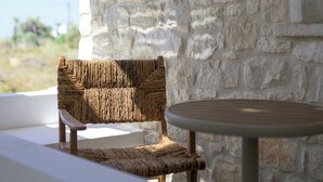 A stone wall with a woven chair and a small round table. - Stone Whisper (Naxos)
