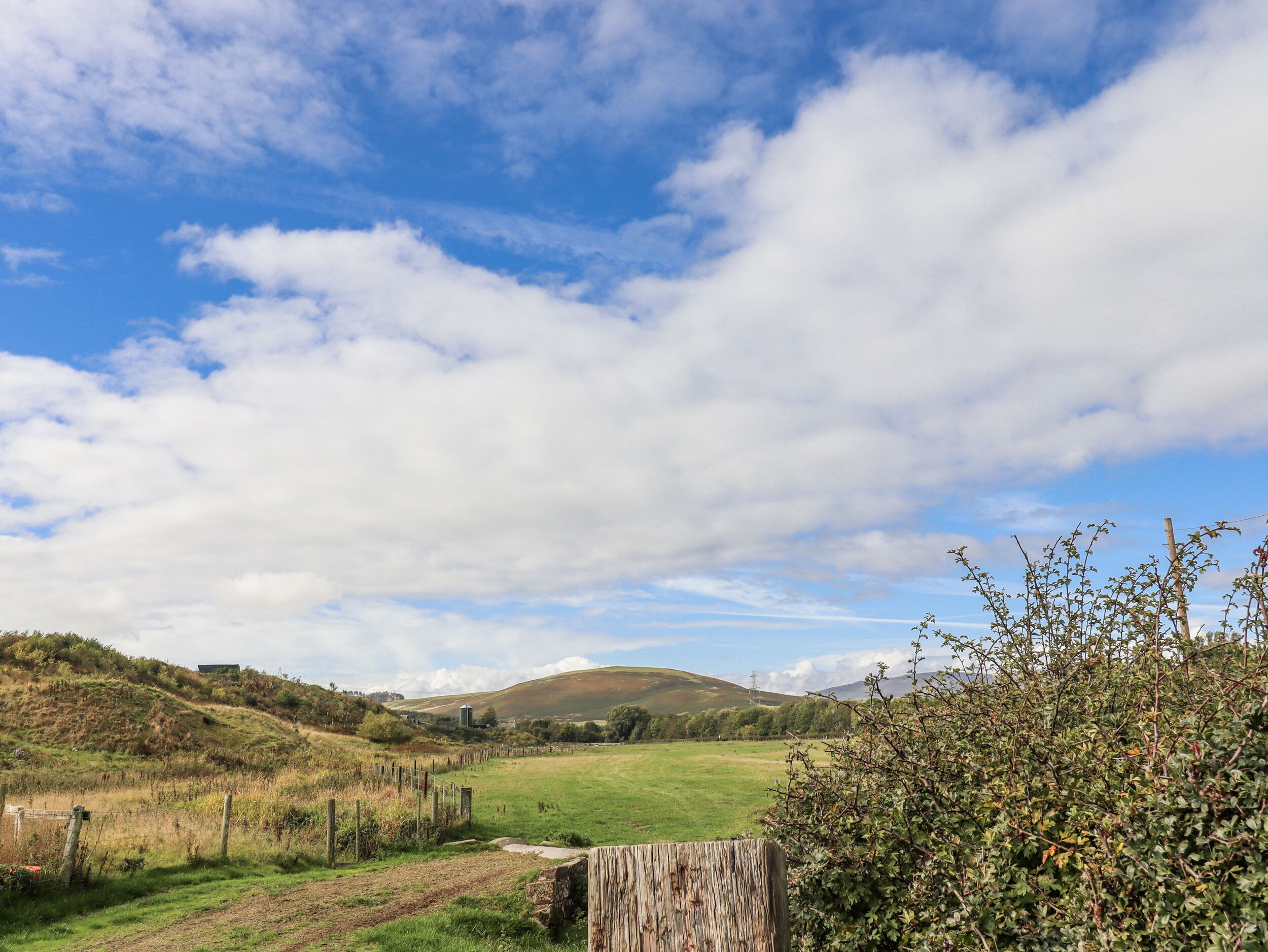 A rural landscape with rolling hills, a fenced field, and a wooden fence.