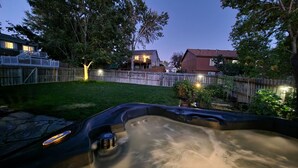 Un jardin avec un jacuzzi, une clôture en bois et des maisons en arrière-plan.