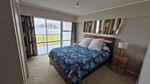 A bedroom with a bed, a nightstand, a lamp, and a view of the outdoors through a sliding door.