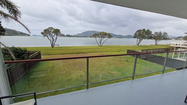 A balcony with a view of a grassy area and a body of water with trees and mountains in the distance.