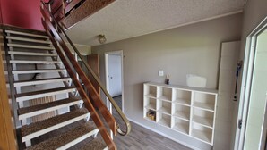 A staircase with wooden steps and a handrail, leading to a room with a white shelving unit and a door.