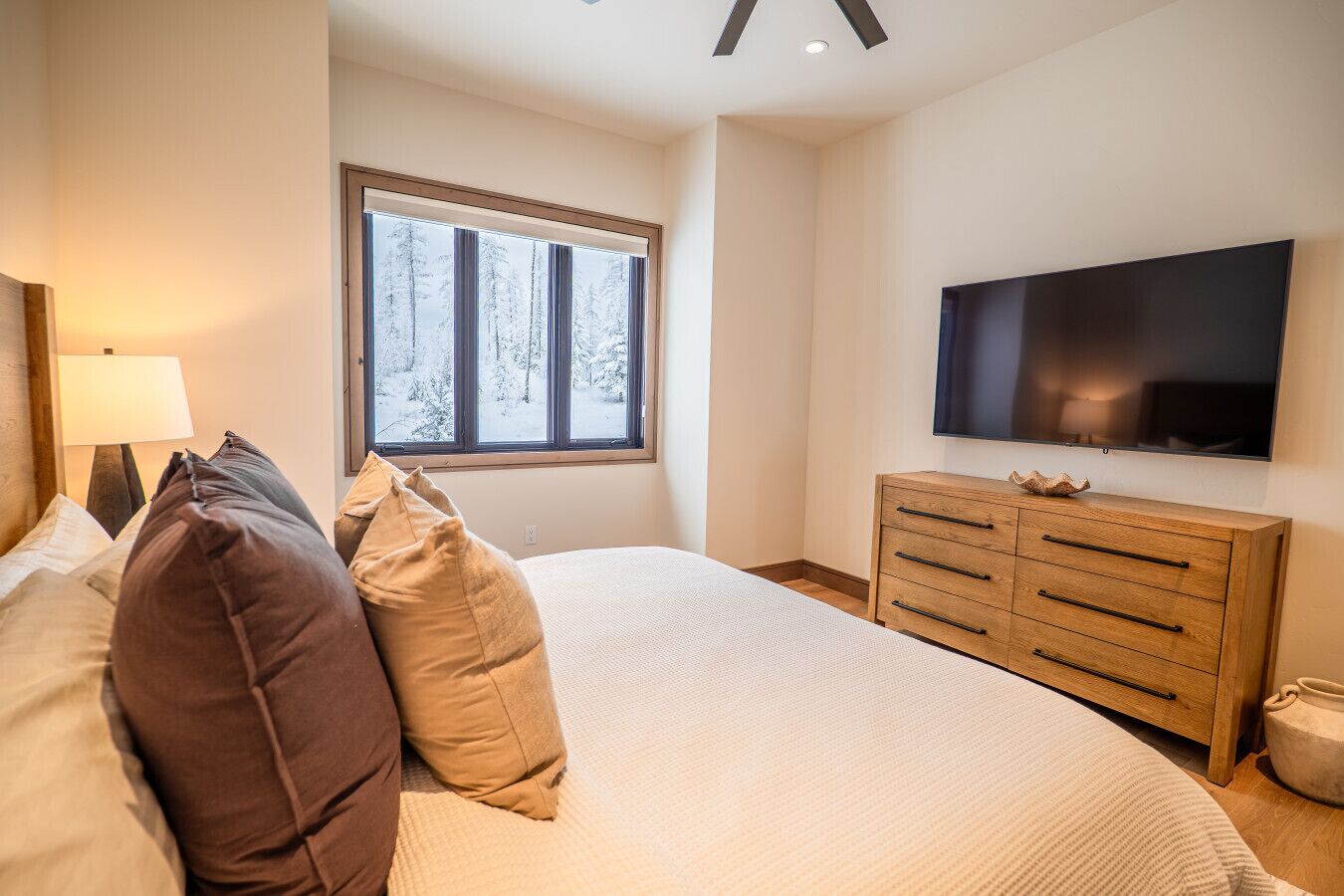 Una camera da letto con un grande letto, una cassettiera in legno, una TV a schermo piatto e una finestra con vista innevata.