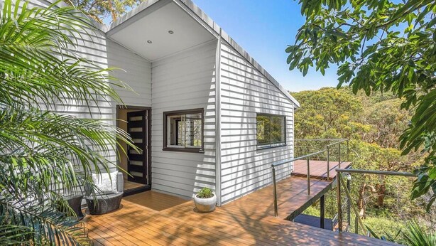 A modern house with a wooden deck, large windows, and a view of the surrounding forest. - Large architect designed home directly overlooking the Royal National Park (Bundeena)