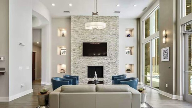 A modern living room with a stone accent wall, a flat-screen TV, a fireplace, and a large window. - River House Condos (Baton Rouge)