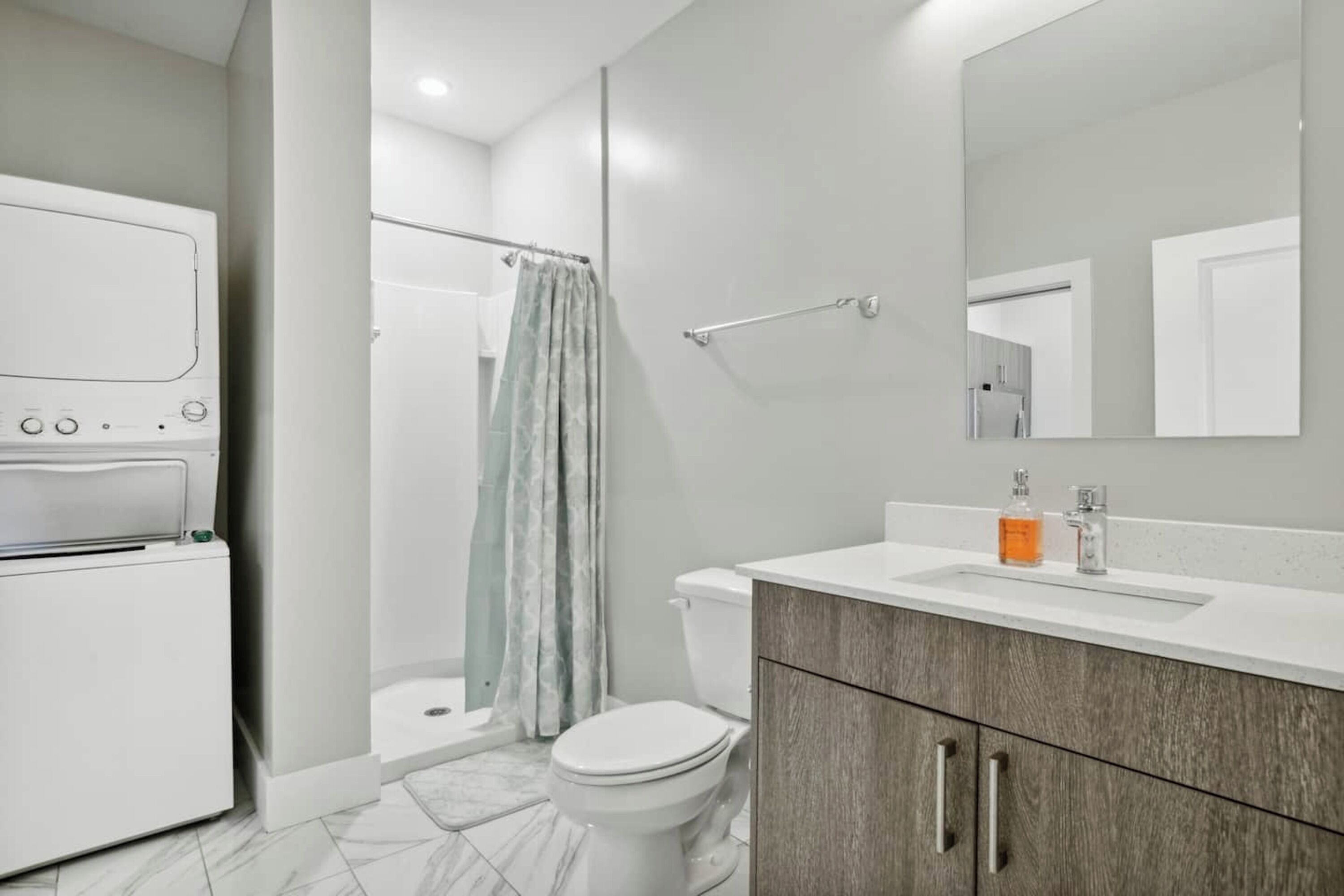 Un baño moderno con inodoro blanco, ducha con cortina, lavabo con espejo y mueble con cajones.