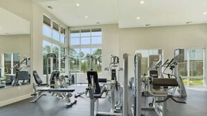 A spacious gym with various exercise machines, large windows, and a high ceiling. - River House Condos (Baton Rouge)