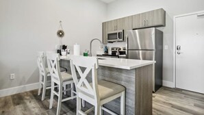 A modern kitchen with a central island, white chairs, and stainless steel appliances. - River House Condos (Baton Rouge)