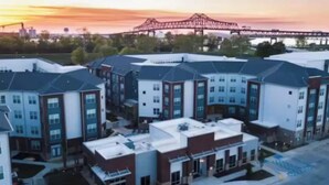 A modern apartment complex with multiple buildings, a parking area, and a bridge in the background. - River House Condos (Baton Rouge)