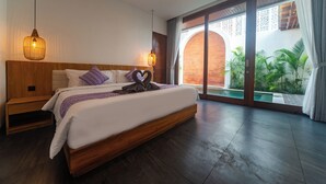 A modern bedroom with a large bed, wooden headboard, and a view of a swimming pool and greenery.