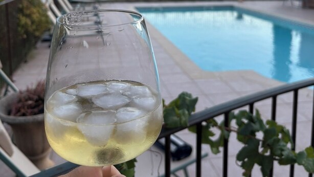 A hand holding a glass of white wine with ice cubes, overlooking a swimming pool with lounge chairs and greenery in the background. - Provencal house with private pool in the heart of Provence Verte - Cotignac (Cotignac)