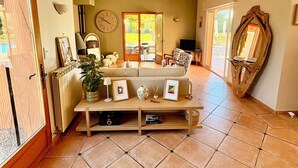 A spacious living room with a large sofa, a coffee table, and a fireplace. There is a large window with a view of the outdoors, and a wooden ceiling. - Provencal house with private pool in the heart of Provence Verte - Cotignac (Cotignac)