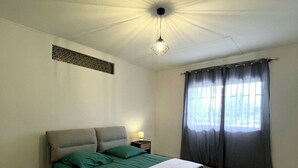 Ein Schlafzimmer mit Bett, Nachttisch, Wandleuchte und einem Fenster mit Vorhängen.