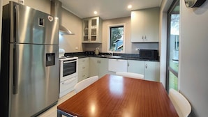 A modern kitchen with stainless steel appliances, white cabinetry, and a wooden dining table. - Cosy Cabin in the Loop (Te Anau)