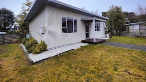 A single-story house with a sloped roof, a front porch, and a small front yard with a gravel pathway and a bush. - Cosy Cabin in the Loop (Te Anau)