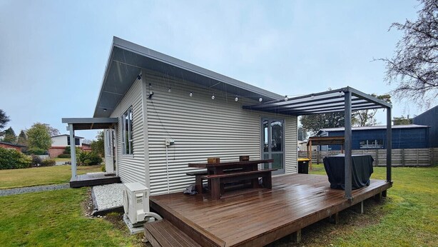 A single-story house with a wooden deck, a covered outdoor seating area, and a small garden. - Cosy Cabin in the Loop (Te Anau)