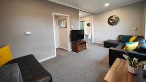 A living room with a black sofa, a wooden coffee table, and a TV on a stand. - Cosy Cabin in the Loop (Te Anau)