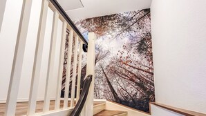 Een trap met houten treden en witte leuningen, die leidt naar een kamer met een groot muurschildering van bomen.
