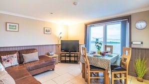 Ein Wohnzimmer mit einer Couch, Fernseher, Esstisch, Stühlen und Meerblick.