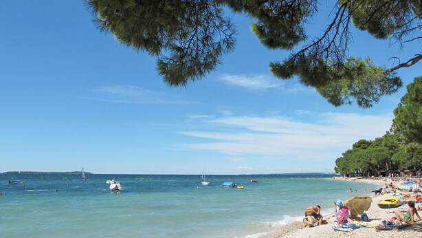 Ein Strand mit klarem Wasser, Kiesufer und einigen Booten.