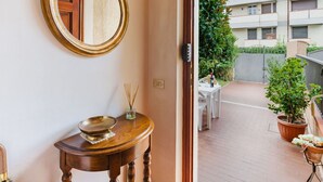 A room with a round mirror, a small wooden table with a bowl and reed diffuser, and a view of a balcony with potted plants and a building in the background. - Wonderful  villa for 8 people with A/C, TV and patio (Viareggio)