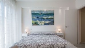 Una camera da letto con un letto, due comodini, un quadro raffigurante una barca a vela e una porta sul lato destro.