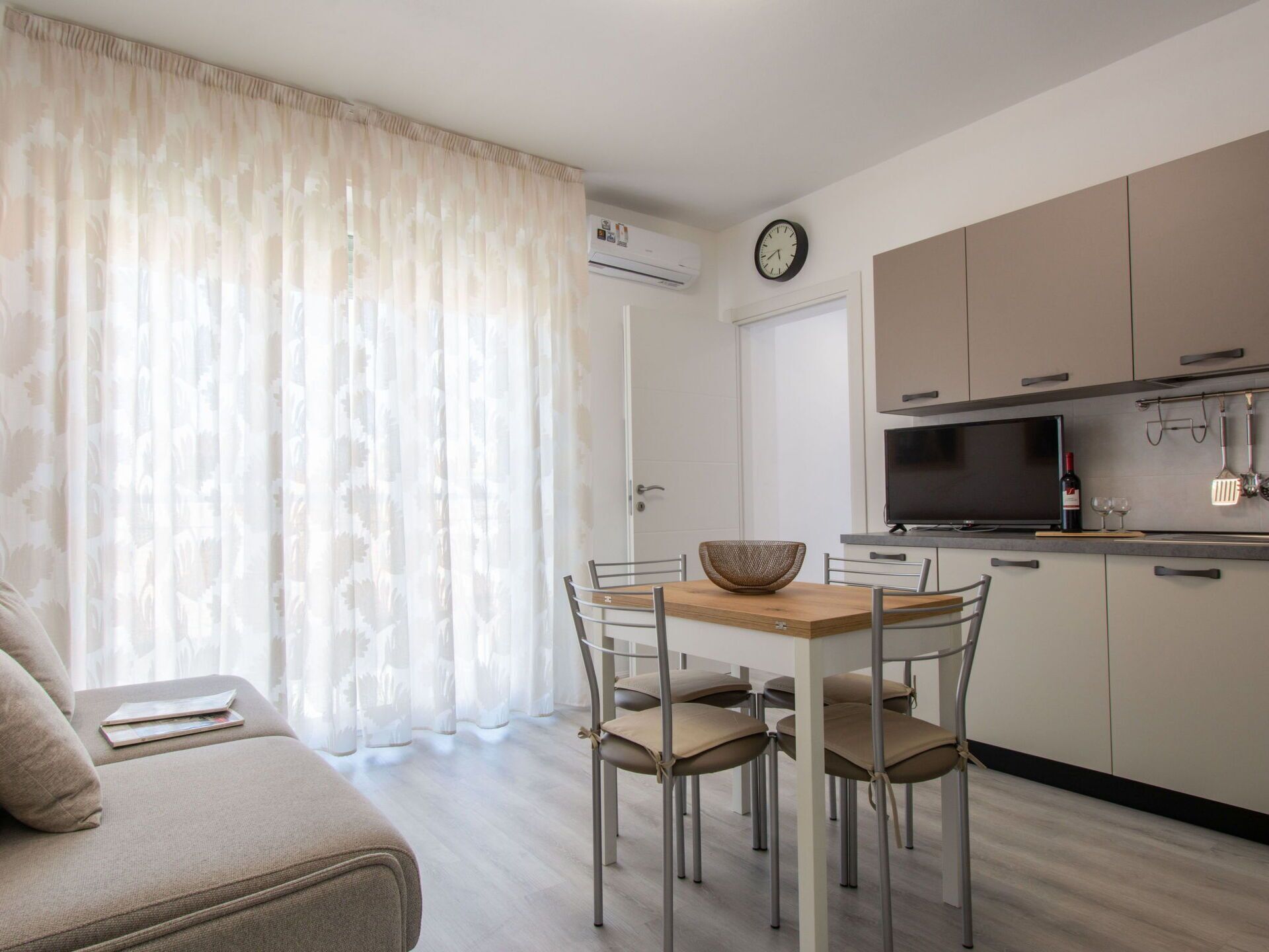 A modern kitchen with a flat-screen TV, a microwave, and a wine bottle on the counter.