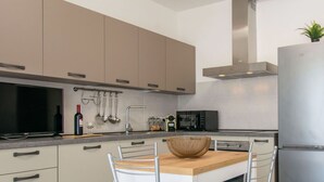 Una cucina moderna con mobili color beige, un frigorifero in acciaio inossidabile, un forno a microonde e un'area pranzo con tavolo in legno e sedie in metallo.
