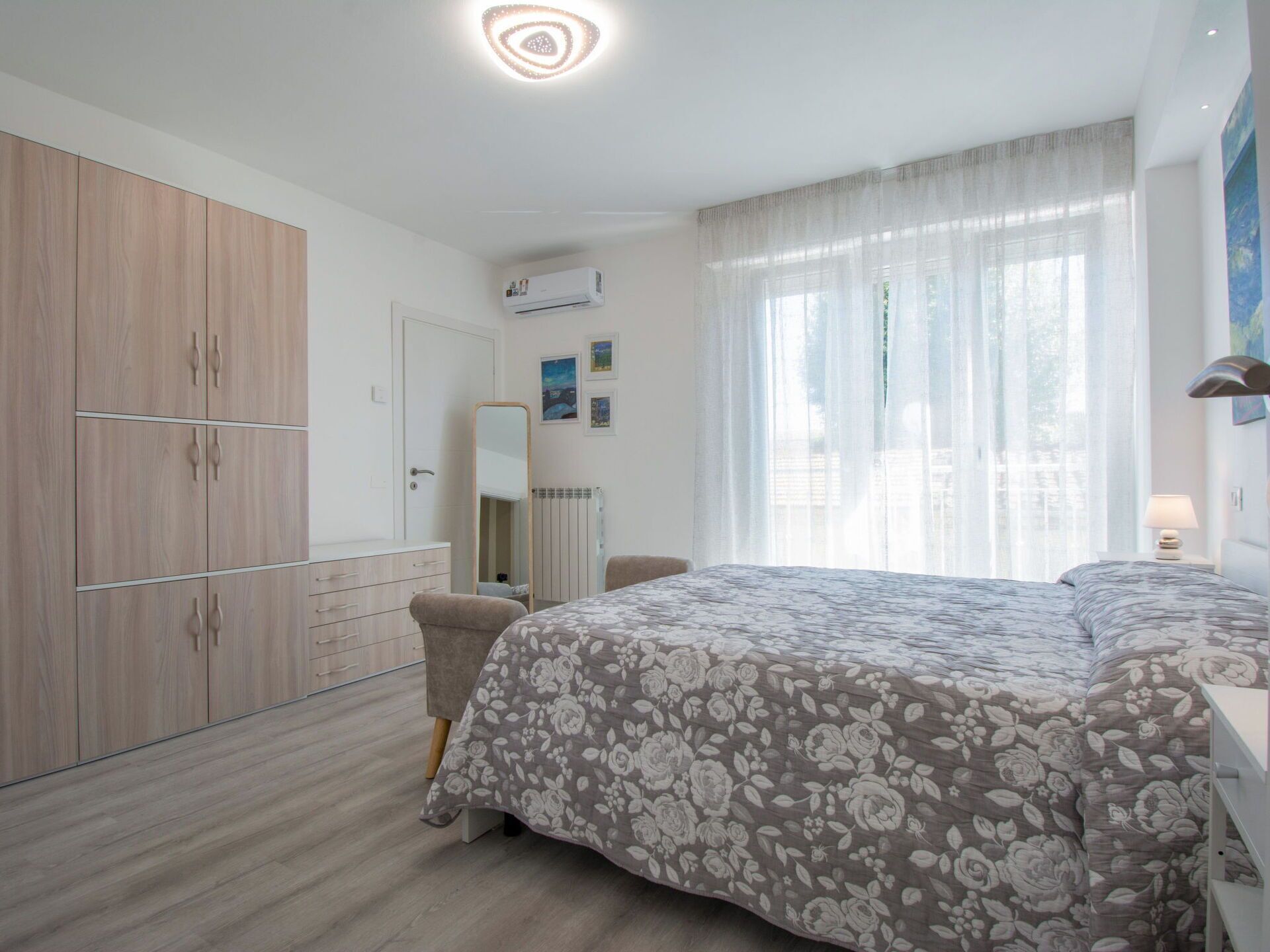 A bedroom with a bed, a wardrobe, a mirror, and a window with curtains.